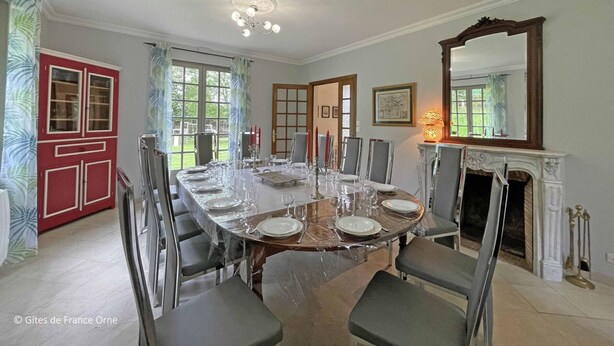 A dining room with a large table set for six, surrounded by chairs. There is a fireplace with a mirror above it, and a window with curtains. - Spacious house for 15 people with garden and pets allowed (Longny-au-Perche)