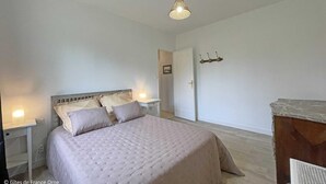 Quarto com cama, abajures, cabeceira de madeira, uma porta e um cabideiro fixado na parede.