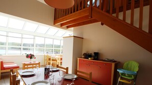 A dining area with a wooden table set for four, a red cabinet, and a high wooden staircase.