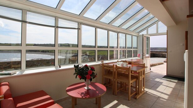 A sunlit room with a large skylight, a dining area with wooden furniture, and a view of a body of water.