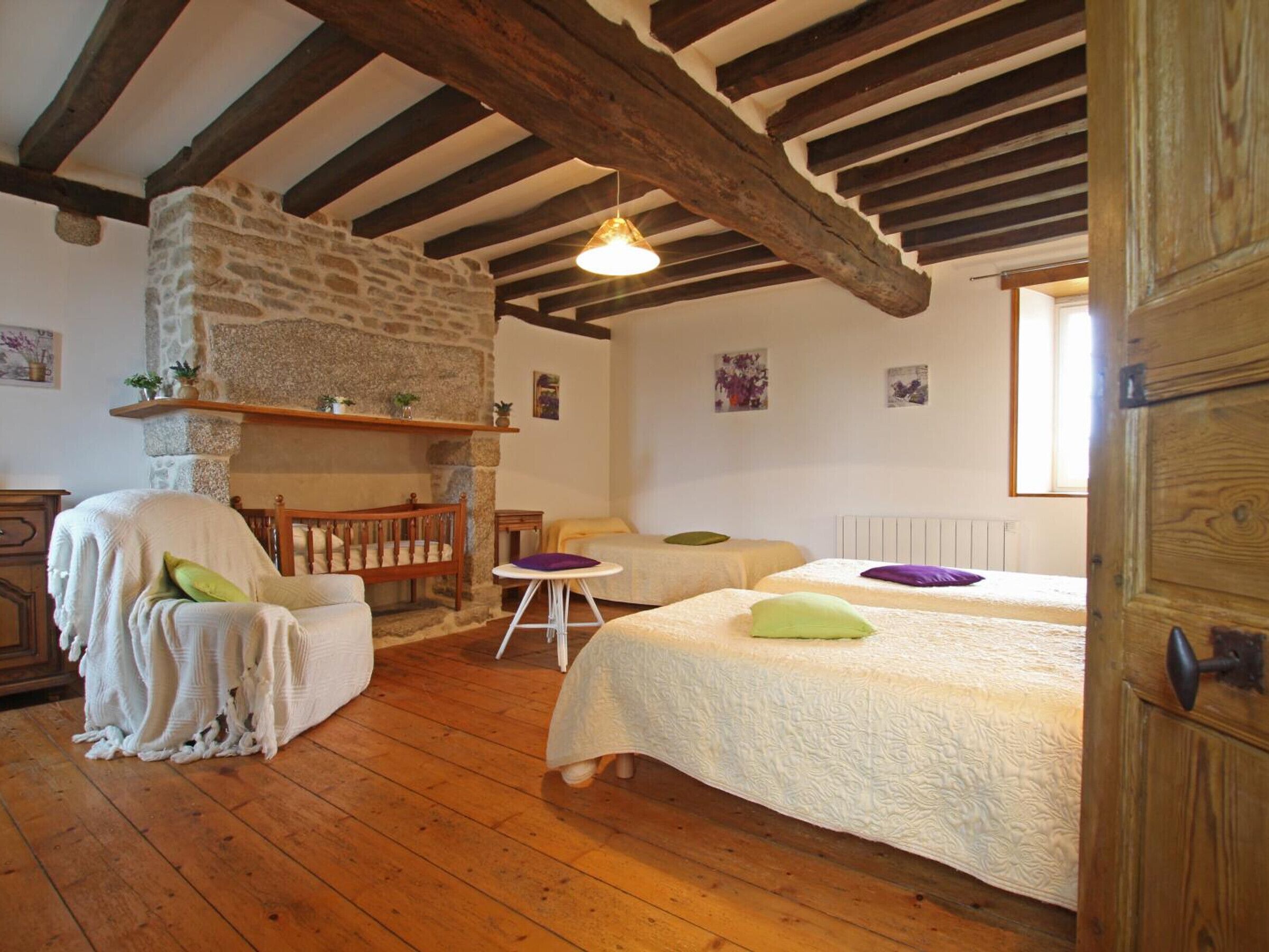 A cozy room with a stone fireplace, wooden beams, two beds, a chair, and a small table.