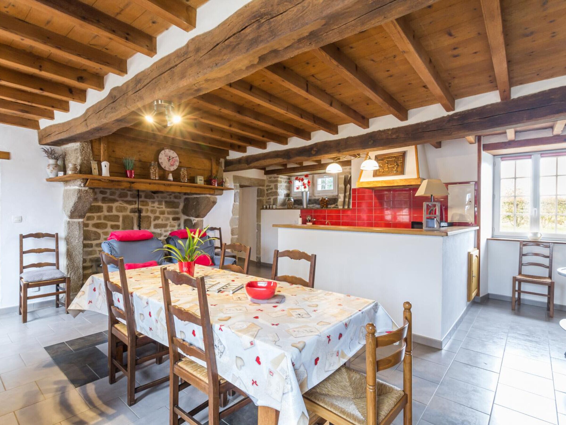 Un comedor rústico con chimenea de piedra, vigas de madera y una cocina al fondo.
