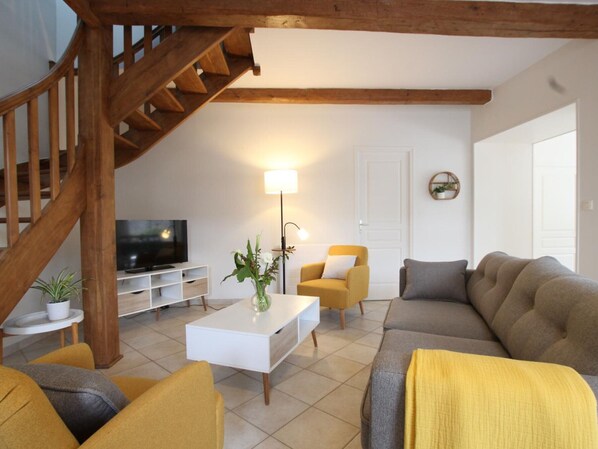 Un salon avec un escalier, un téléviseur, une table basse ornée d’un vase et deux canapés.