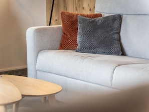 A light grey sofa with two cushions, one brown and one grey, and a small round wooden table in front. - Luxurious 3BR Apartment for 8, 50m from Slopes & Lift in Montalbert, WiFi, Parking (La Plagne Montalbert)
