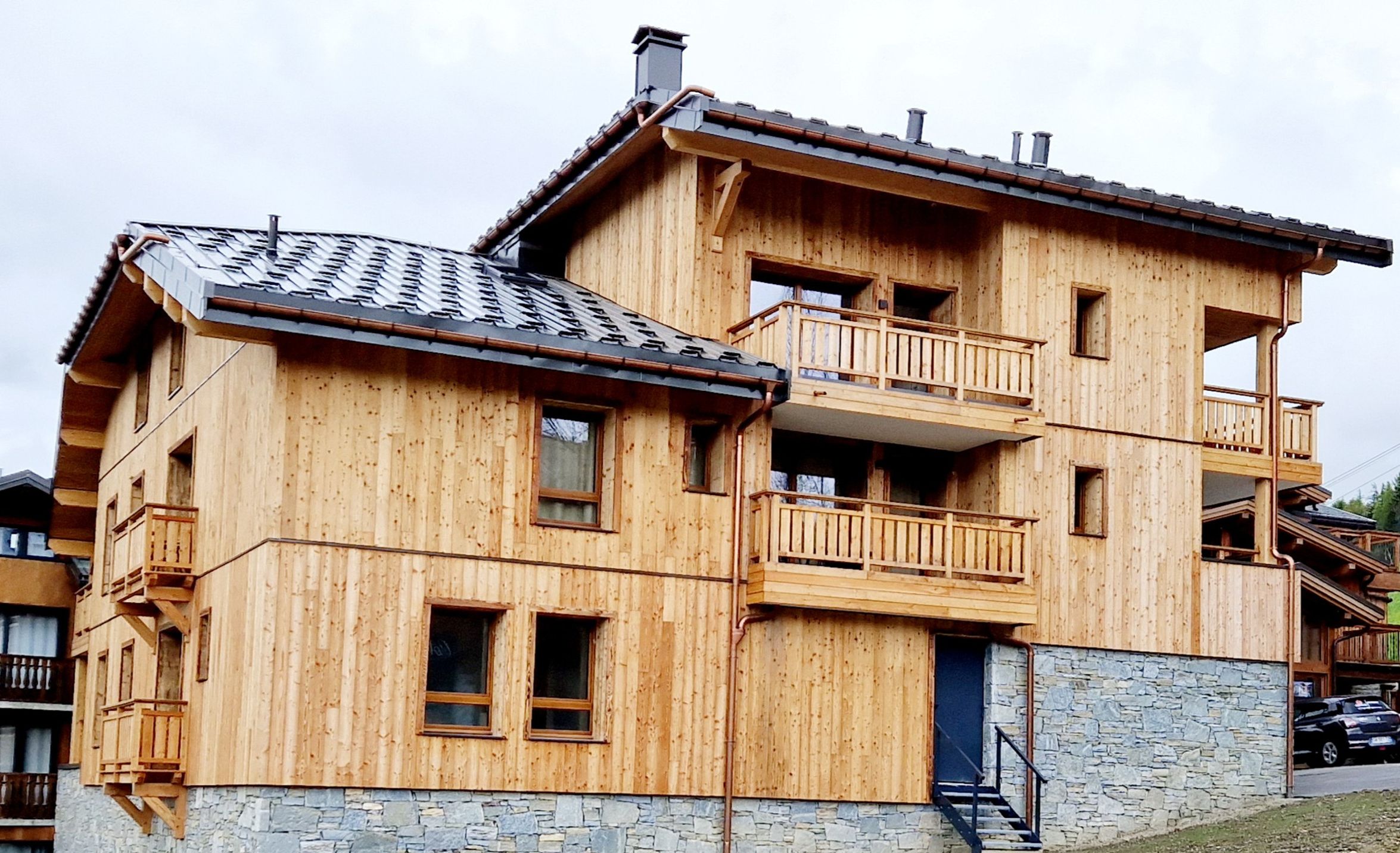 Una cabaña de madera de varios pisos con balcones, cimientos de piedra y techo de metal.