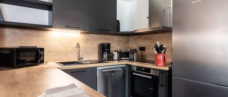 A modern kitchen with a stainless steel refrigerator, a microwave, a coffee maker, and a dishwasher.