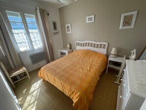 Et soveværelse med seng, sengeborde, en stol og et vindue med gardiner.