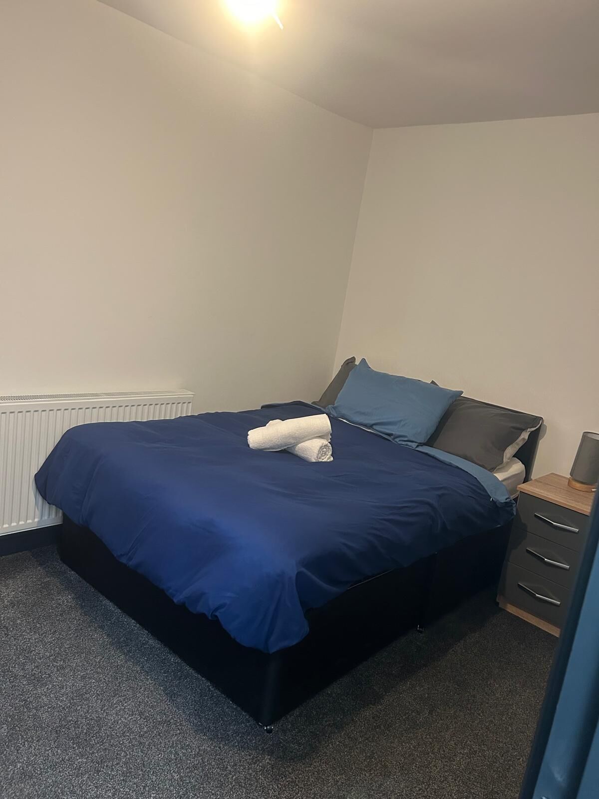 A bedroom with a bed, a nightstand, and a radiator.
