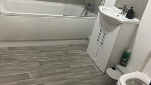 Un baño moderno con ducha de vidrio, una bañera blanca, un lavamanos con espejo y un inodoro.