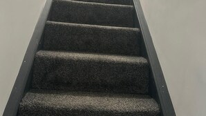 Una escalera con peldaños alfombrados y barandales de metal, que conduce a un espacio luminoso en la parte superior.