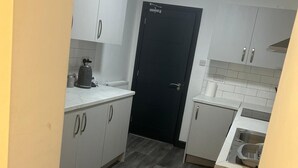 Una cocina compacta con armarios blancos, una puerta negra y un suelo gris.