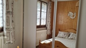 A bedroom with a wooden bed, a window with curtains, and a radiator. - 2-Room Apartment in Châtel - 5 People (Châtel)