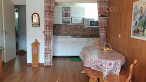 A compact kitchen with white cabinets, a microwave, and a sink. A dining table with a patterned tablecloth and a basket of apples is in the foreground. - 2-Room Apartment in Châtel - 5 People (Châtel)