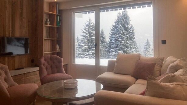 A modern living room with a glass coffee table, a sofa, and a chair. There is a bookshelf with books and a television mounted on the wall. - 4-room apartment, 8 people, parking, ski slopes (Saint-Gervais-les-Bains)