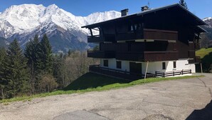 A two-story chalet with a balcony, set against a backdrop of snow-capped mountains. - 4-room apartment, 8 people, parking, ski slopes (Saint-Gervais-les-Bains)