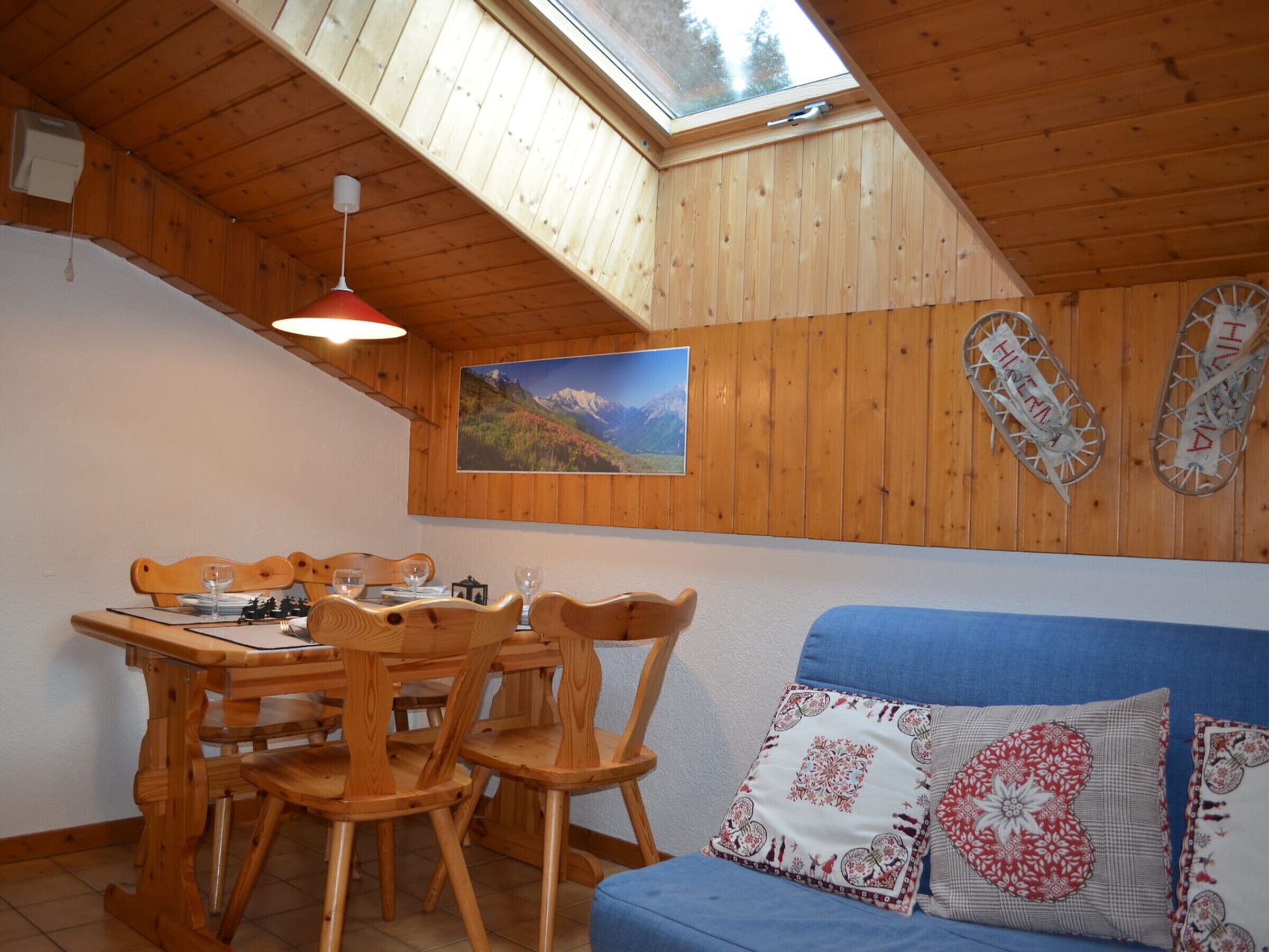 A wooden interior with a dining table, chairs, a blue sofa, and a skylight.