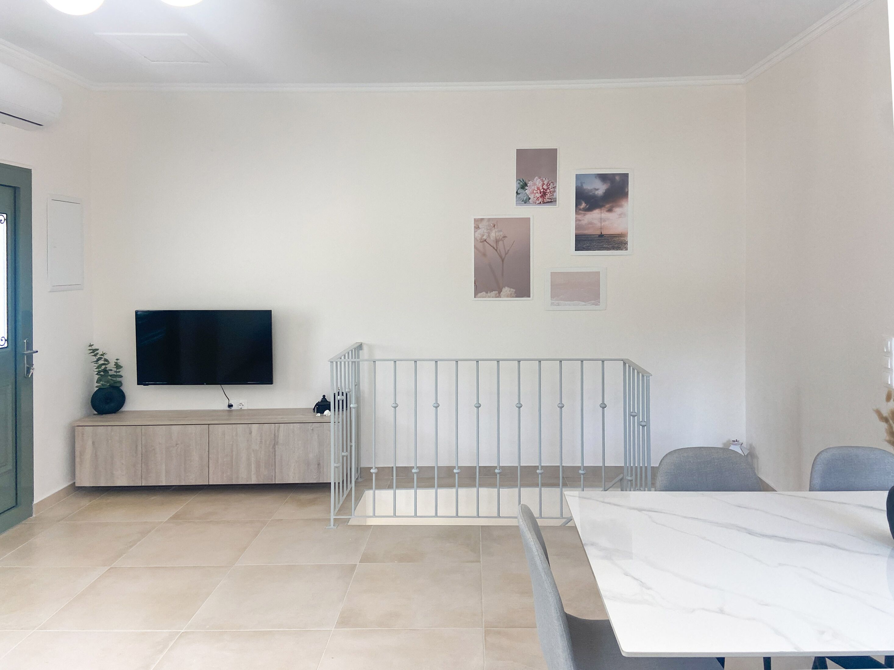 Una sala de estar moderna con televisor, una cuna blanca, una mesa de comedor y algunas fotografías enmarcadas en la pared.