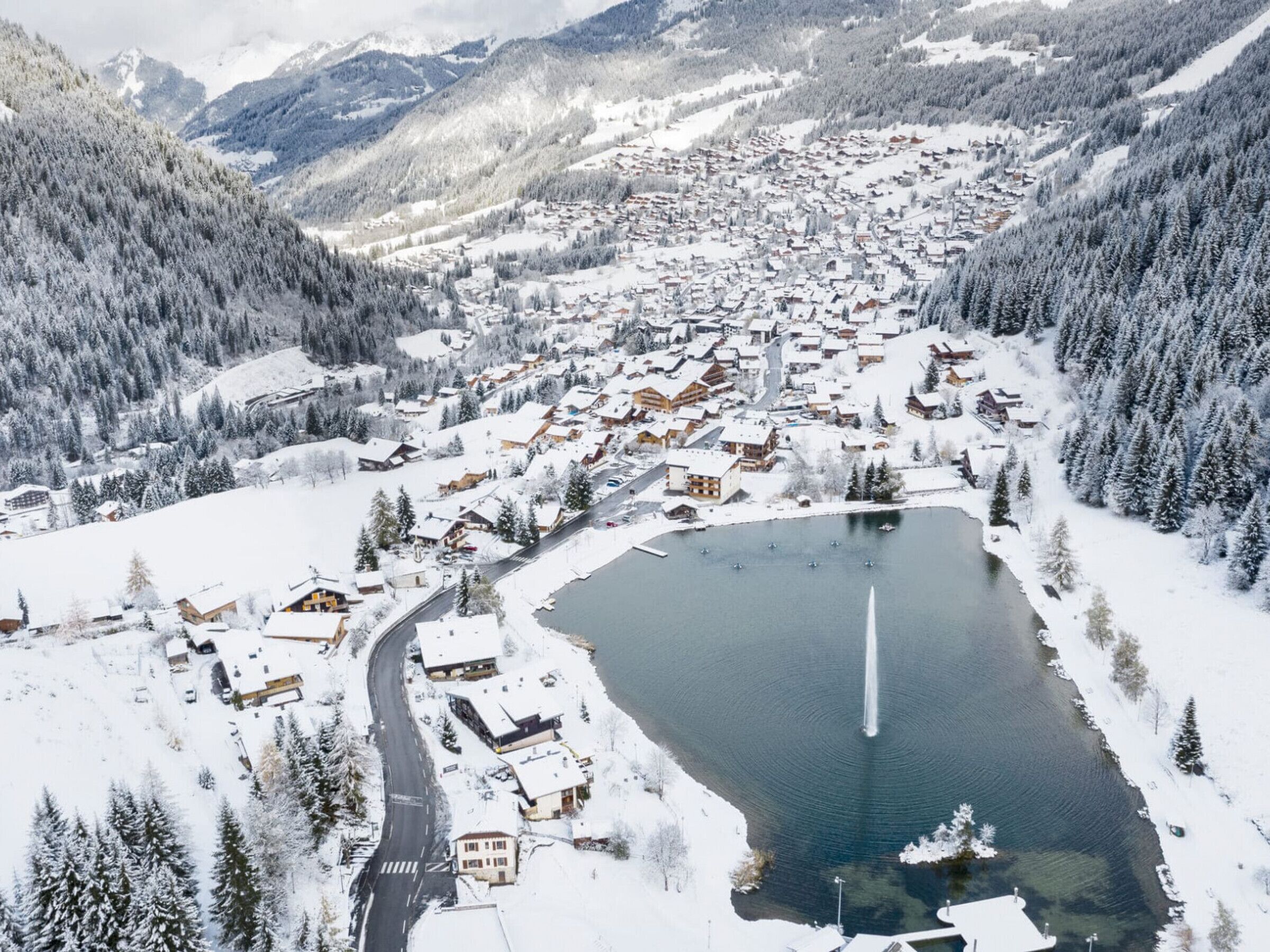 Eine verschneite Stadt mit einem zentralen See, umgeben von bewaldeten Bergen.
