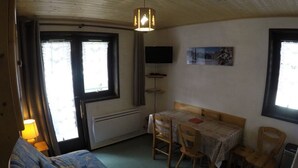 A small, cozy room with a bed, a table with chairs, a heater, and a TV on the wall. - Studio for 4 with balcony, pets allowed and parking (Châtel)