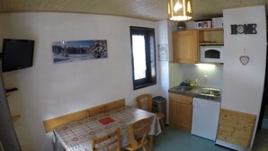 A compact kitchen with wooden cabinets, a dining table with chairs, a refrigerator, and a microwave. - Studio for 4 with balcony, pets allowed and parking (Châtel)