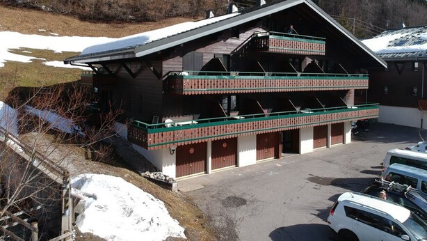 A chalet-style building with a sloped roof, wooden balconies, and a parking area with two cars. - Studio for 4 with balcony, pets allowed and parking (Châtel)