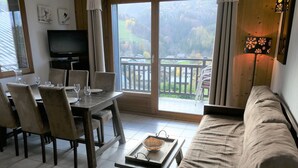 Un salón con sofá, mesa de comedor, sillas, televisor y balcón con vistas al campo.