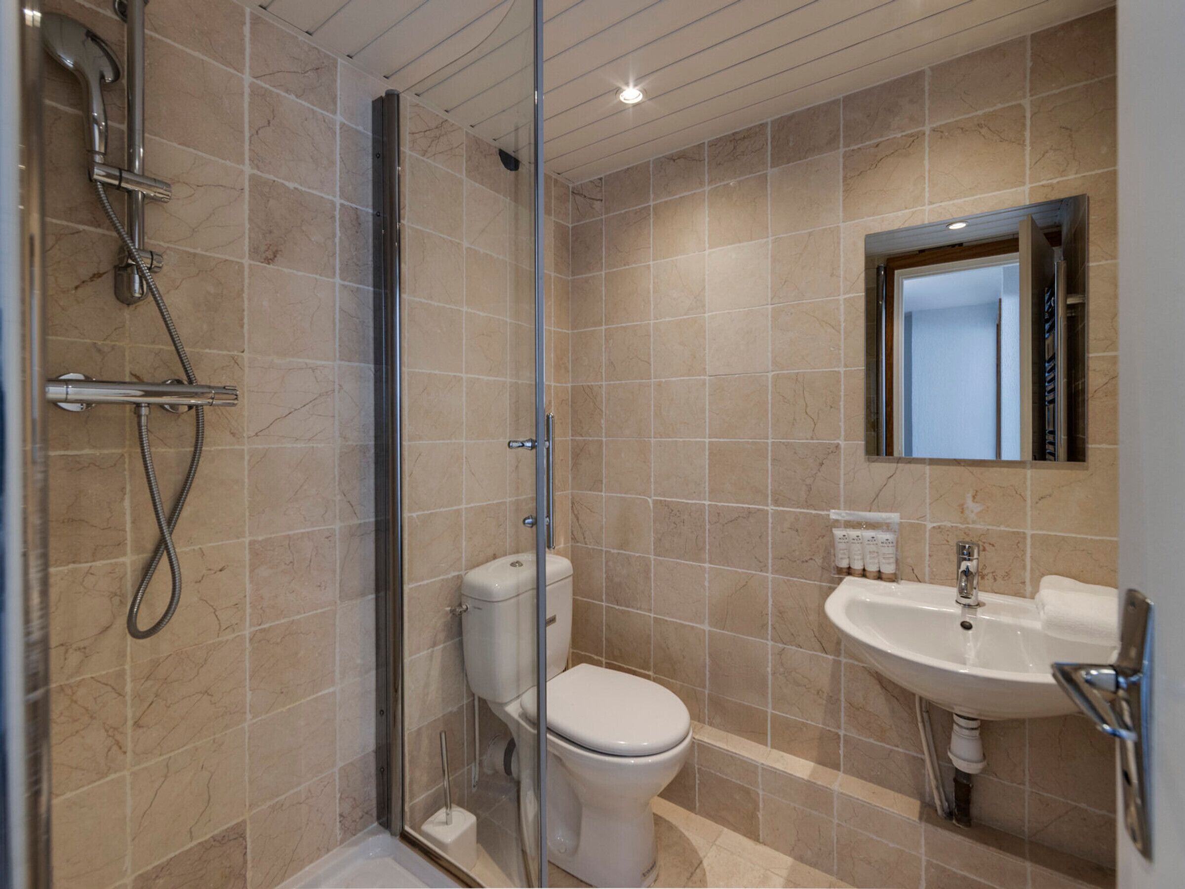 A modern bathroom with a glass-enclosed shower, a toilet, and a sink with a mirror above it.