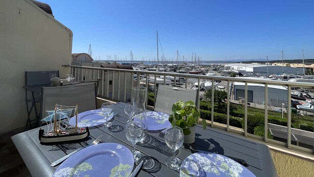 Mesa de comedor para cuatro personas con vista a un puerto deportivo y barcos al fondo.