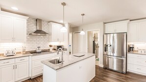 A modern kitchen with white cabinetry, a stainless steel refrigerator, and a granite countertop island. - Punta Gorda Isles waterfront pool home (Punta Gorda)