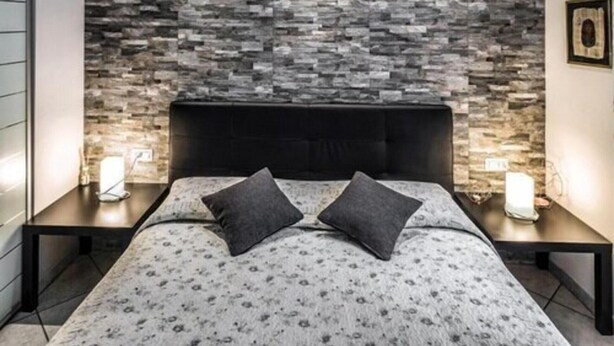 Une chambre moderne avec une tête de lit à motifs de pierre, un lit recouvert d’une couette à fleurs et deux lampes de chevet.
