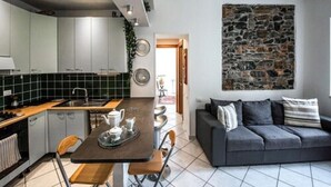Une cuisine moderne avec des meubles gris, un mur d’accent en pierre, un coin repas avec une table et des chaises, et un canapé gris dans l’espace salon.