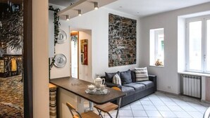 Un salon moderne avec un canapé, une table à manger et des chaises, un mur en pierre et une fenêtre laissant entrer la lumière naturelle.