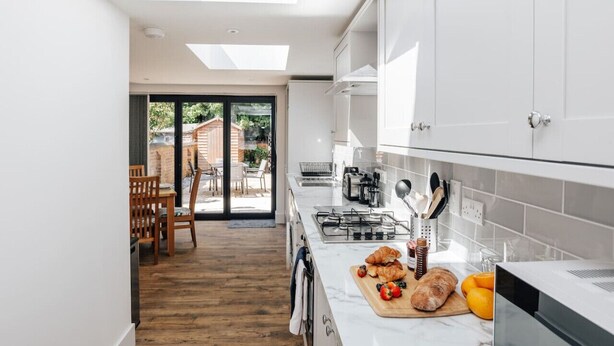 Una cocina moderna con tragaluz, una zona de comedor con sillas de madera y vista a un patio.