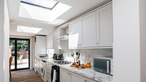 Una cocina moderna con armarios blancos, horno empotrado, microondas y tragaluz.