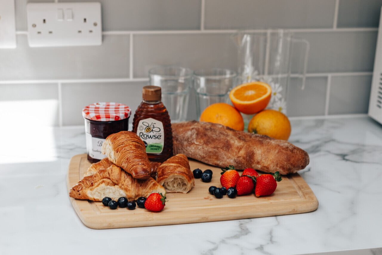 Eine Küchenarbeitsplatte mit Croissants, Honig, Erdbeeren, Blaubeeren und Orangen.