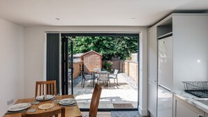 Una cocina compacta con comedor, puerta corrediza de vidrio que da a un patio con mobiliario exterior y un cobertizo de madera.