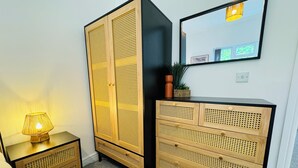 A room with a wooden wardrobe with perforated panels, a matching nightstand, and a mirror on the wall. - Spacious One Bed Apt With Scenic Views (Ventnor)