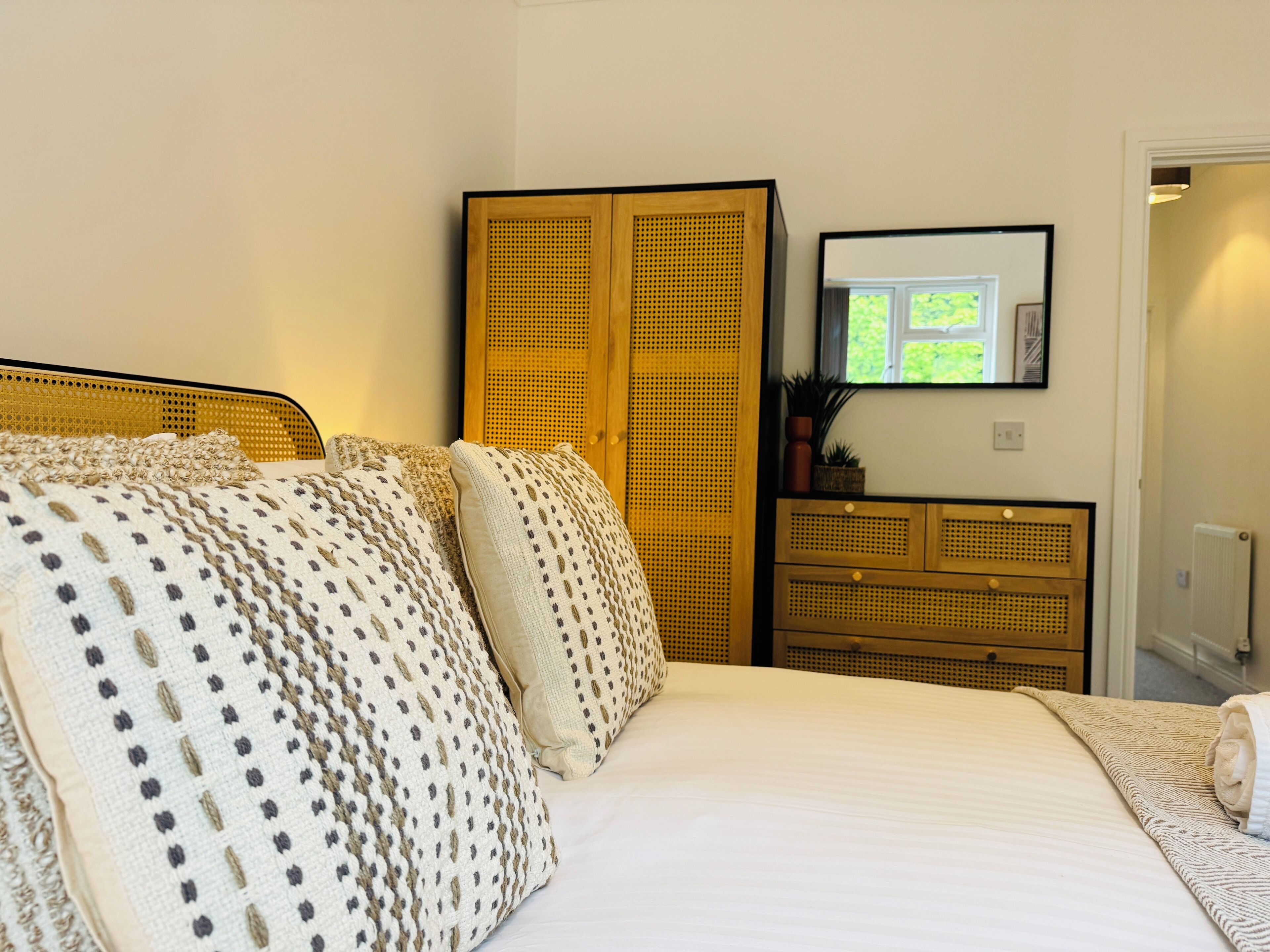 A bedroom with a bed, a wooden wardrobe, a dresser, and a framed picture on the wall.