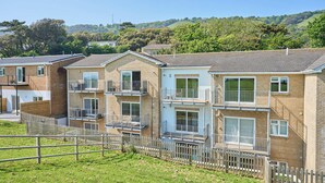 A row of brick apartment buildings with balconies, a wooden fence, and a hilly landscape in the background. - Spacious One Bed Apt With Scenic Views (Ventnor)