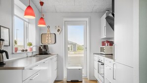 A modern kitchen with white cabinets, a stainless steel sink, a coffee maker, and a microwave. There are two pendant lights, a trash bin, and a view of the outside through a door. - 3 bedroom lovely home in Ringkøbing (Ringkøbing)