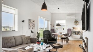 A modern living room with a sofa, coffee table, and chairs. There is a dining area with a table and chairs. The room has large windows and a ceiling fan. - 3 bedroom lovely home in Ringkøbing (Ringkøbing)