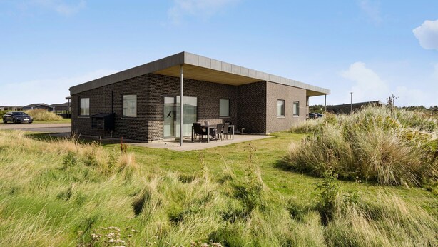 A modern two-story house with a brick exterior, a flat roof, and a covered patio area with outdoor furniture. - 3 bedroom lovely home in Ringkøbing (Ringkøbing)