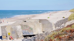A beach with a concrete structure, people, and tents. - 3 bedroom lovely home in Ringkøbing (Ringkøbing)