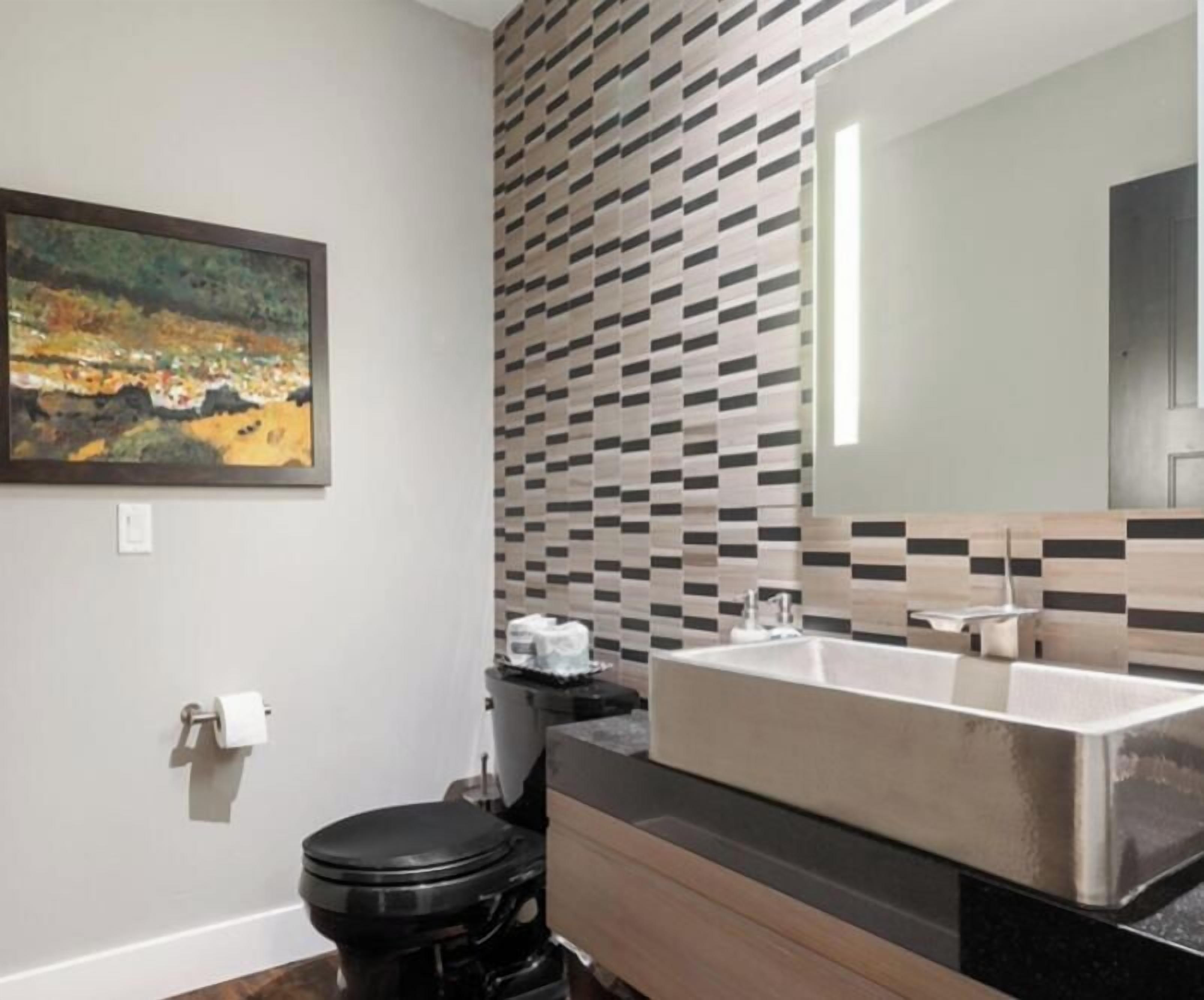 A modern bathroom with a black toilet, a sink with a mirror, and a tiled backsplash.