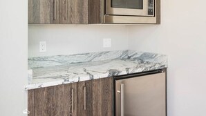 A kitchen with wooden cabinets, a marble countertop, a stainless steel microwave, and a dishwasher. - Park Haus on Main Street in Historic Old Town (Park City)