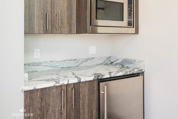 A kitchen with wooden cabinets, a marble countertop, a stainless steel microwave, and a dishwasher.
