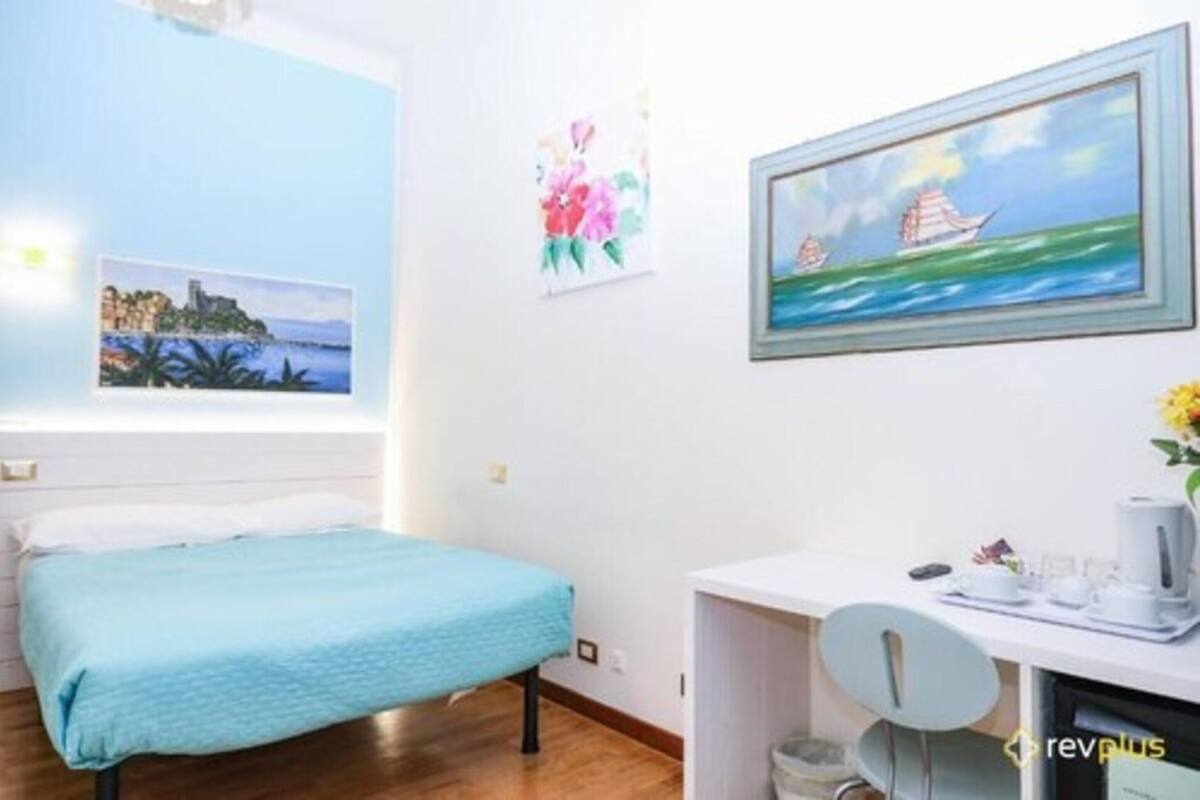 Een kamer met een bed, een bureau en een stoel. Er hangen schilderijen aan de muur.