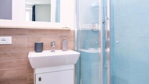 A bathroom with a white sink, a mirror above it, and a glass shower enclosure. - Lia Rooms (La Spezia)