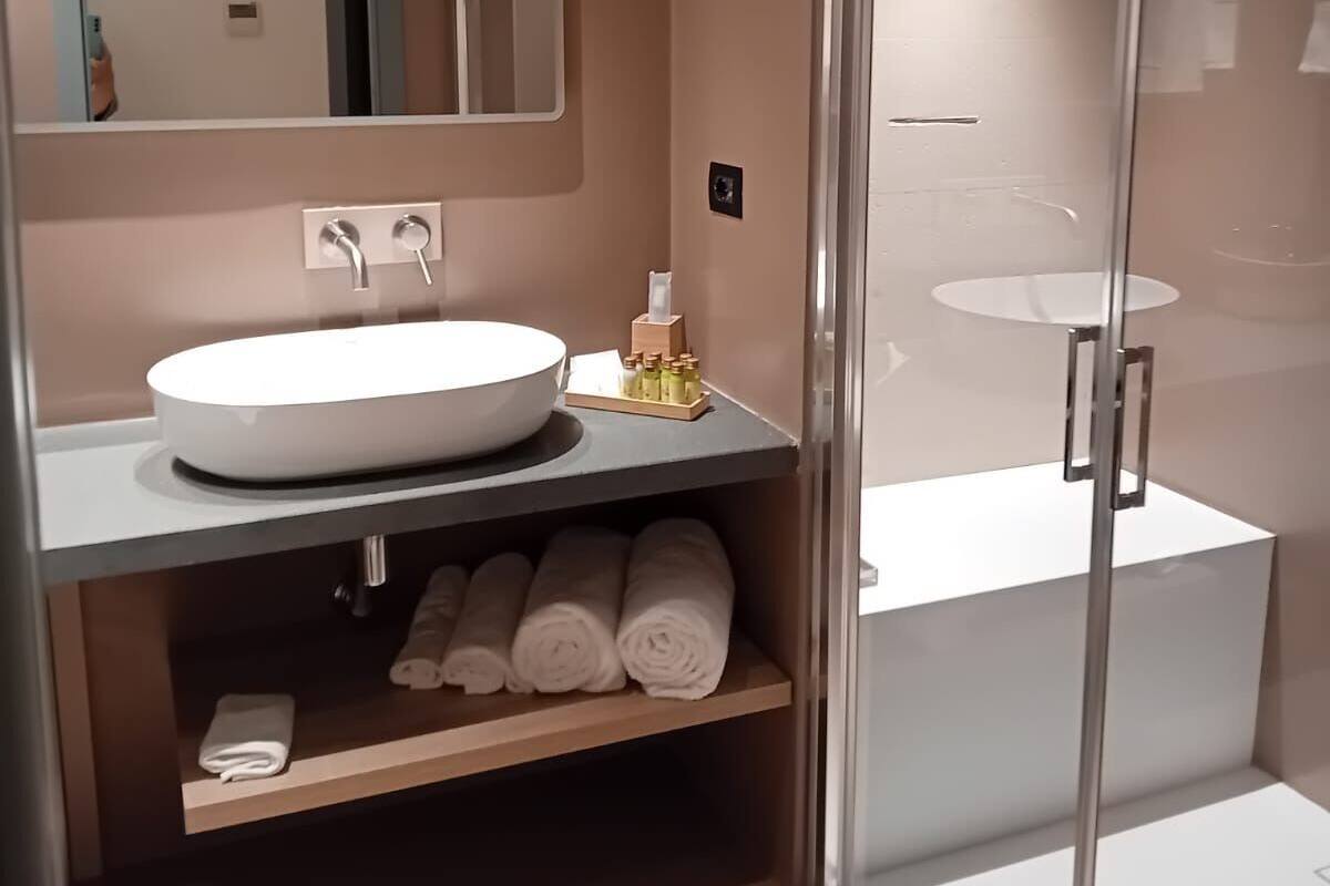 A modern bathroom with a large mirror, a round sink, and a glass-enclosed shower.