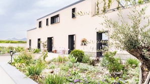 A modern building with a flat roof, multiple windows, and a garden with various plants and flowers. - Bahal dell Etna (Ramacca)